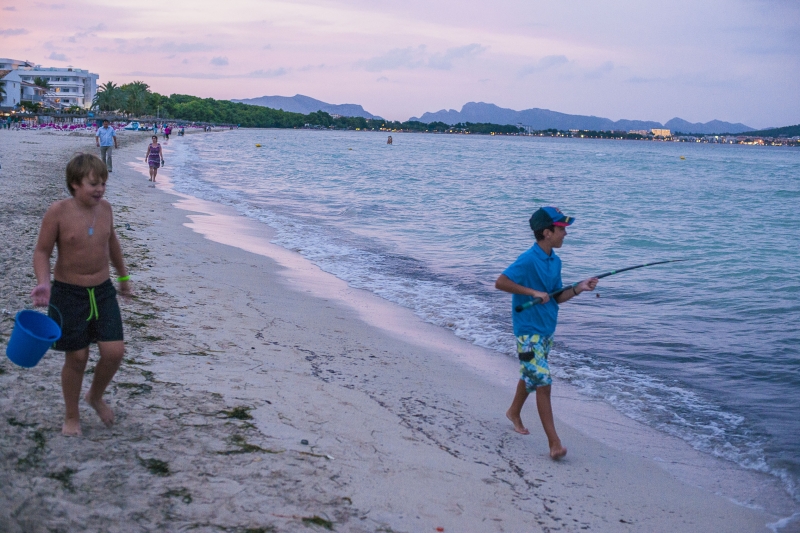Child with bucket and another child with fishing on the beach