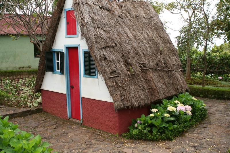 Small house with roof and red door in a green setting