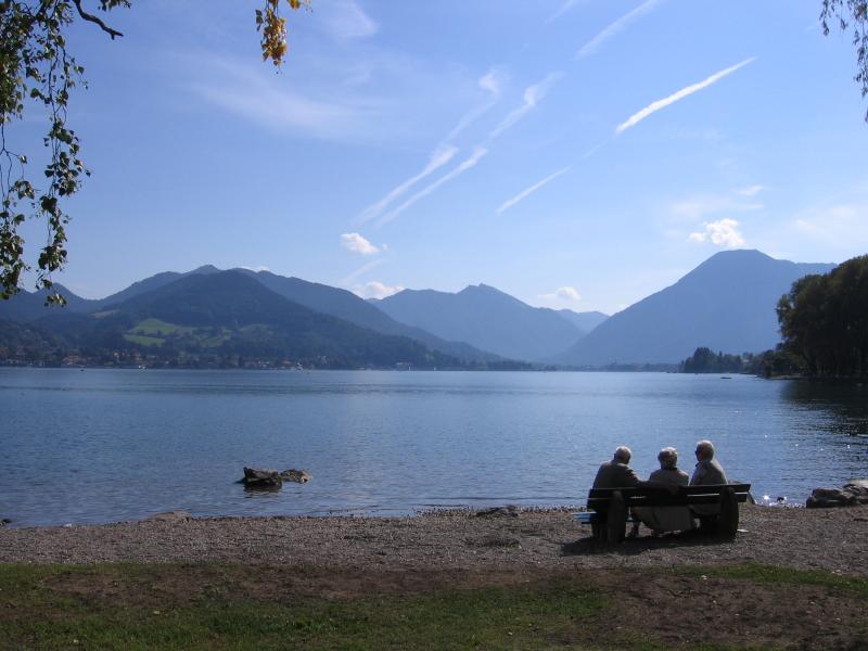 Three people sitting on the lakefront in front of a mountain landscape