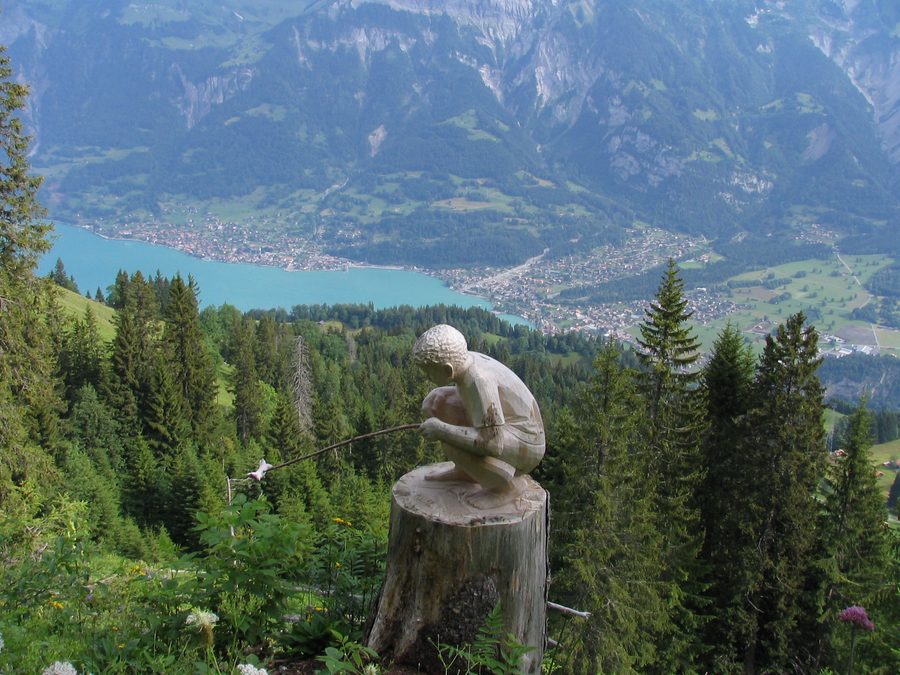 Carved wooden figure on the Schnitzlerweg trail in Axalp with Brienz in the background