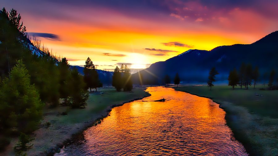 Sunset over Yellowstone National Park with warm light and clouds above the landscape.