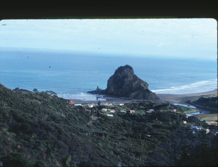 Piha Beach with black sand, surf, and rocky headlands.