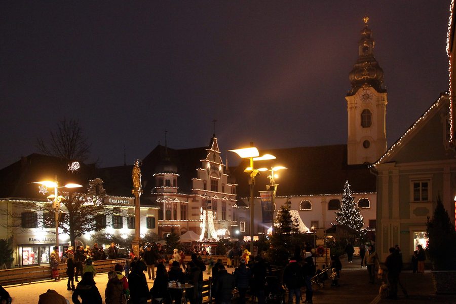 Illuminated main square in Hartberg with historic buildings, Marian column, town hall, and parish church of Saint Martin